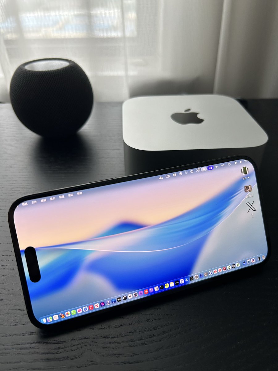 An iPhone in landscape acting as a Mac display, sitting beside a Mac mini and a HomePod mini